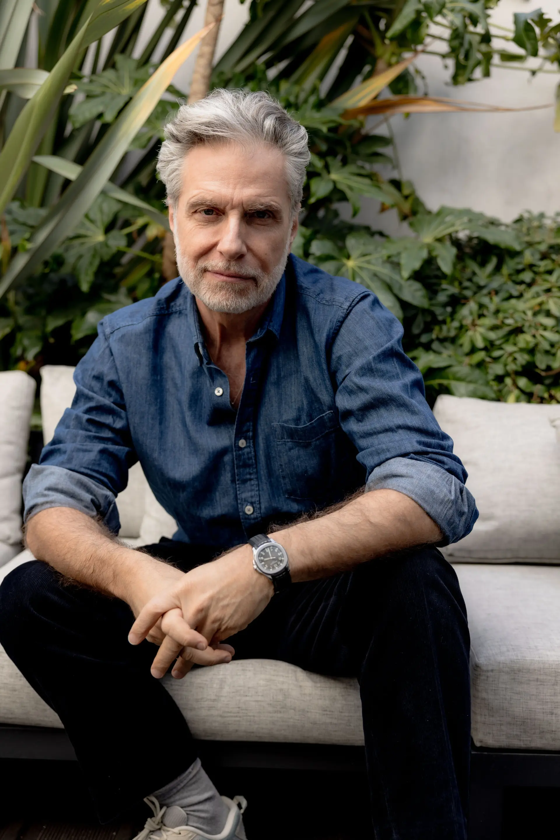 Portrait de Jean Pierre Marois, propriétaire de l'Hôtel Les Bains, qui porte une chemise en jean bleu, et une montre et un pantalon noir