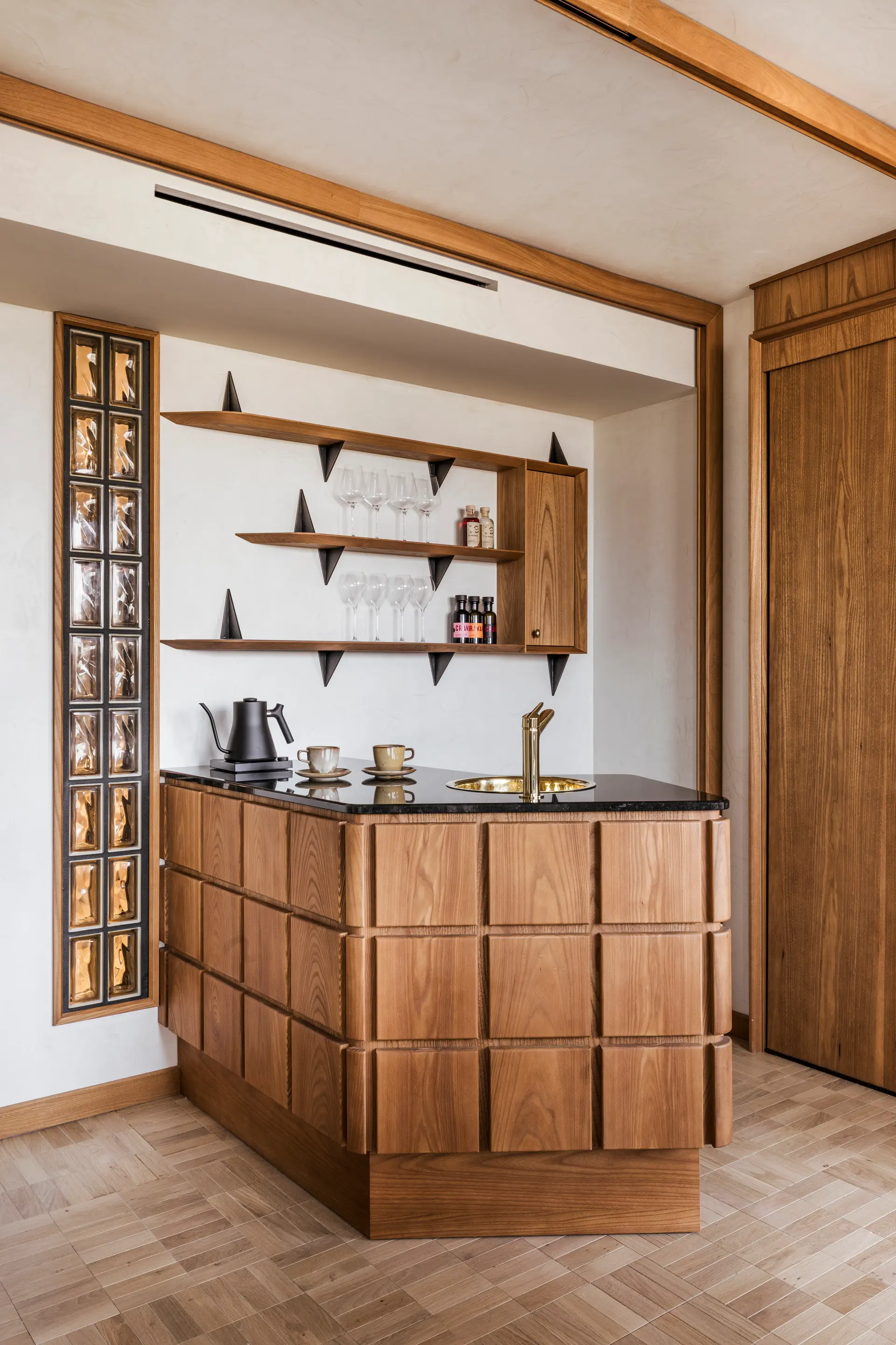 Bar privé dans la suite de l'Hôtel en bois clair avec des accessoires visibles et des étagères en fond